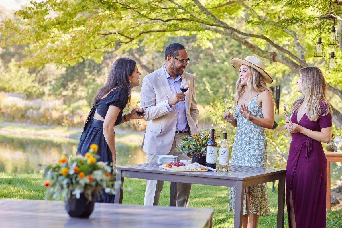 Three women and one man with wine outside socializing